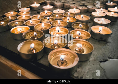 La masterizzazione memorial candele su sfondo scuro. numerose rotonde memorial candele in portacandele. Un fuoco che brucia sulle candele in piedi sulla tavola. Foto Stock