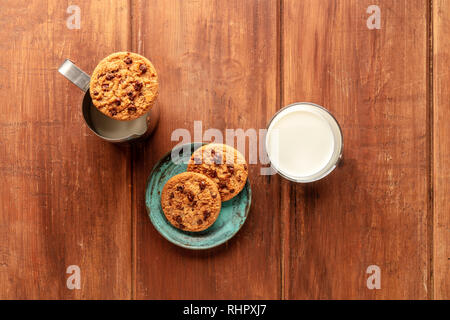 Una foto aerea di biscotti al cioccolato al buio su un rustico sfondo di legno con il latte e lo spazio di copia Foto Stock