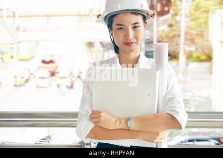 Donna ingegnere indossare il casco di sicurezza e design stand di carta al lavoro del sito Foto Stock