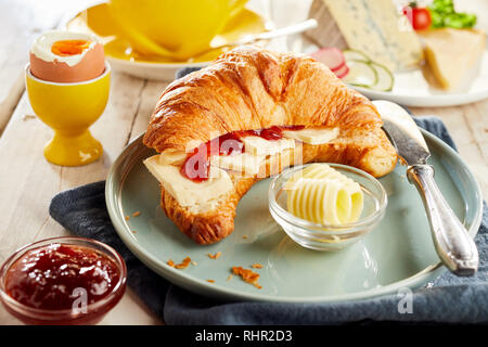 Croissant ripieni di formaggio e ketchup, servita su piastra in ceramica con riccioli di burro e soft-uova sode. Ristorante table vista da vicino Foto Stock