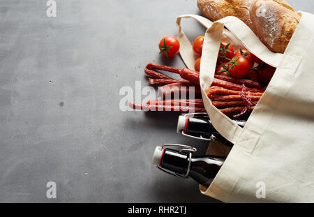 La birra artigianale, salsiccia piccante e baguette in una eco-friendly tessuto riutilizzabile shopping bag su ardesia con spazio di copia Foto Stock