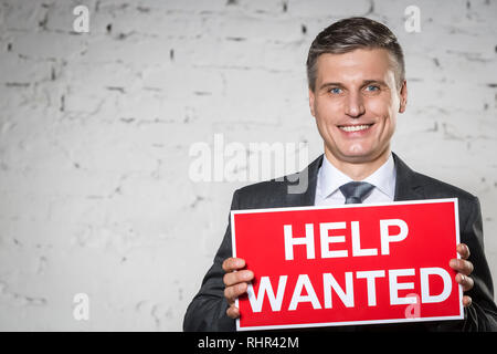 Ritratto di imprenditore sorridente azienda aiuto voluto firmare mentre in piedi contro il bianco muro di mattoni Foto Stock