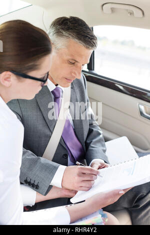 Imprenditore firma di documenti durante la seduta dal collega in auto Foto Stock