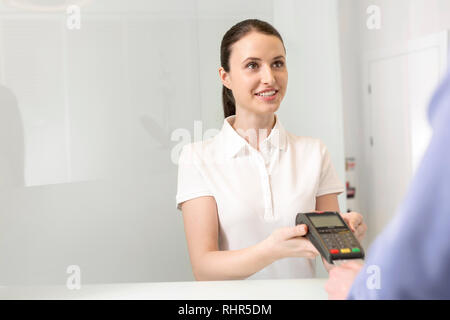 Sorridente paziente giovane pagamento mediante carta di credito presso la cassa in clinica Foto Stock