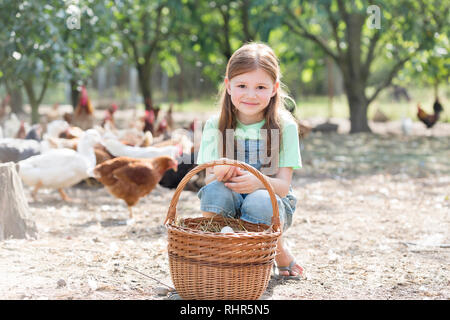 Ritratto di ragazza carina con le uova nel paniere contro i polli a livello di azienda Foto Stock