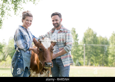 Ritratto di Coppia sorridente in piedi con la mucca in fattoria Foto Stock