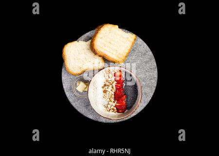 Una sana prima colazione. Cereali di riso o porridge con fragole fresche, mandorla e scaglie di noce di cocco, servita con pane e burro. Isolato sul nero Foto Stock