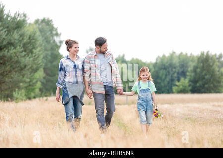 Famiglia camminando sul campo erboso contro sky presso l'azienda Foto Stock