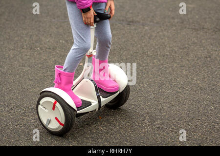 Close-up di bambino ragazza gambe in rosa luminoso stivali di gomma equitazione segway sulla soleggiata strada asfaltata spazio copia dello sfondo. La moderna tecnologia, bambini safet Foto Stock