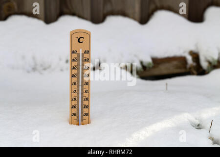 Termometro in legno in piedi nella neve, che mostrano una bassa temperatura, spazio per il testo a destra. L'inverno prossimo concetto. Foto Stock