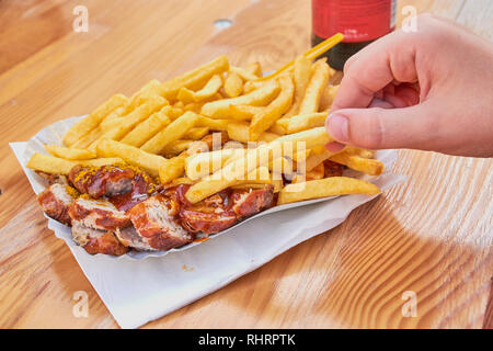 La mano del bambino sta prendendo le patatine fritte con il tedesco salsiccia Currywurst con curry ketchup su una tabella di colore marrone Foto Stock