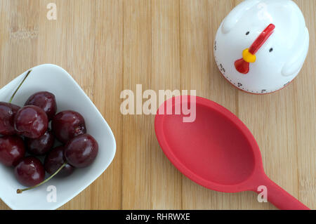 Bella e deliziosa ciliege rosse con un gallo timer sullo sfondo di legno Foto Stock