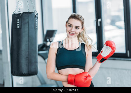 Felice bella ragazza sportiva in guantoni da pugilato sorridente in telecamera in palestra Foto Stock