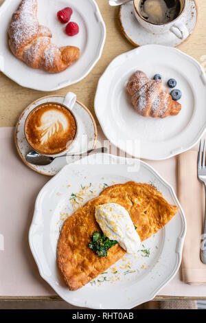 La prima colazione. Frittata - omelette italiano. Frittata con pomodori, avocado, spinaci e formaggio morbido. Cornetti, caffè e altri piatti sul tavolo Foto Stock