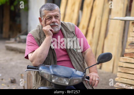 Nice outdoor ritratto del barbuto senior uomo seduto su uno scooter ed essendo in malinconia Foto Stock