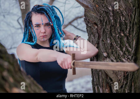 Bellicosi ragazza con i capelli blu dreadlocks nel bosco tra gli alberi. Viking donna con una spada in un abito nero Foto Stock