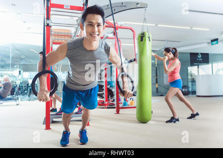 Montare il giovane uomo che esercitano con anelli di ginnastica in un moderno centro fitness Foto Stock