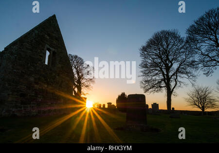 East Lothian, Scozia, Regno Unito, 4 febbraio 2019. Regno Unito: Meteo il sole irrompe attraverso sagome delle pareti in rovina di Gladsmuir vecchia chiesa parrocchiale e il cimitero con lapidi antiche al tramonto in inverno Foto Stock