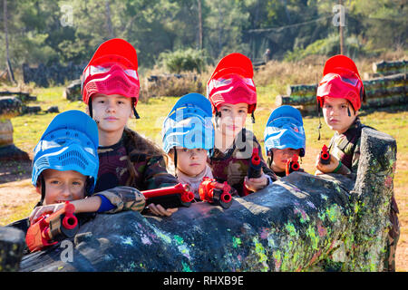 Gentile lieto allegro sorridente gruppo di bambini paintball giocatori in camuffamento in posa con pistole di paintball sul campo da gioco all'aperto Foto Stock