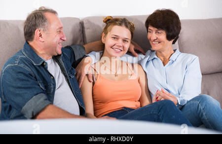 Donna sorridente con i suoi genitori sono in appoggio sul divano di casa. Foto Stock