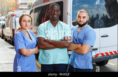 Ritratto di positiva cordiale sorridente ambulanza efficiente team di tre piedi vicino ambulanza Foto Stock