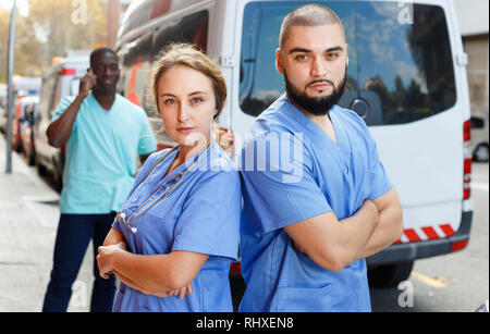 Due positivi friendly sorridente efficiente paramedicals fiducioso in uniforme in posa in prossimità di ambulanza Foto Stock