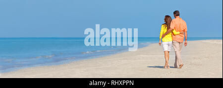 Banner Web panorama vista posteriore di un uomo e di una donna coppia romantica in abiti colorati a camminare su una deserta spiaggia tropicale con un luminoso cielo blu chiaro Foto Stock