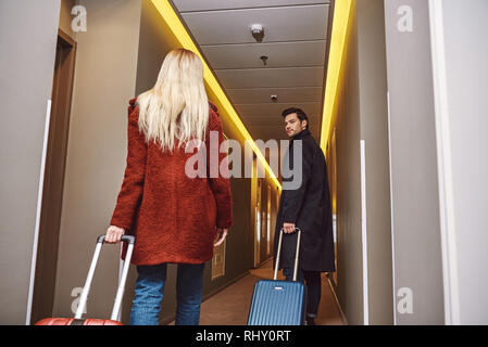 Coppia di viaggiatori nella hall. Vista posteriore dei giovani a entrare al pavimento dell'hotel con i loro bagagli e avente una chat Foto Stock