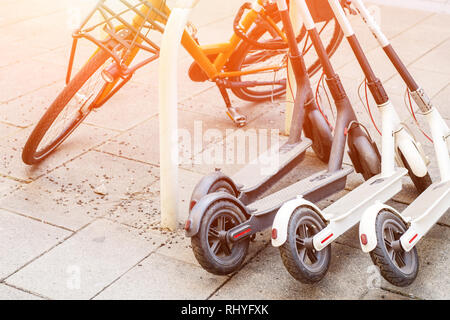 Biciclette e scooter elettrici parcheggiato sulla strada della citta'. Self-service di trasporto strada servizio di noleggio. Noleggio veicolo urbano con applicazione dello smartphone Foto Stock