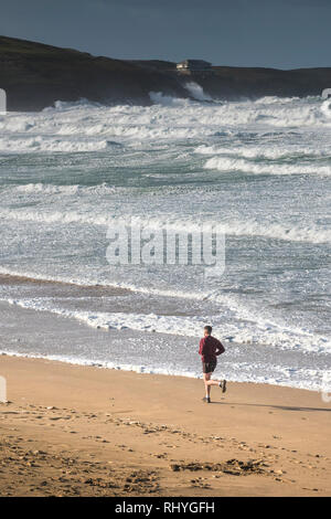 Un uomo che corre lungo il litorale su Fistral Beach in Newquay Cornwall. Foto Stock