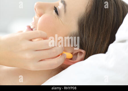In prossimità di una donna mano mettendo i tappi per le orecchie a dormire su un letto di casa Foto Stock
