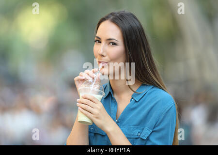 Donna felice bere latte shake con una cannuccia in strada guardando a voi Foto Stock