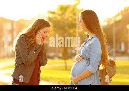 Stupiti ragazza guardando il suo amico in gravidanza pancia in un parco al tramonto Foto Stock