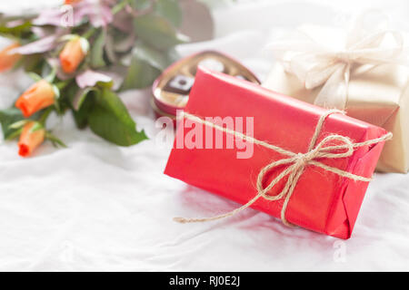 Bella colorato piuttosto dono o presenti in una carta naturale con praline di cioccolato, caffè e rose fresche su un letto. Vacanza, il giorno di san valentino o su Foto Stock