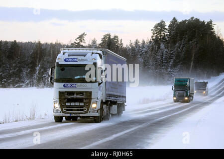 Salo, Finlandia - 18 Gennaio 2019: Bianco Volvo FH di Rutomcargo, Germania, verde autocarro Scania e un viaggio in autobus attraverso il finlandese paesaggio invernale al tramonto. Foto Stock