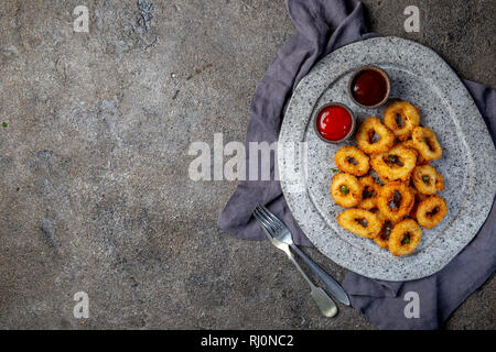 Calamari fritti anelli in pietra grigia piastra con salse. Grigio sfondo concreto Foto Stock