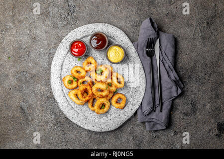 Calamari fritti anelli in pietra grigia piastra con salse. Grigio sfondo concreto Foto Stock