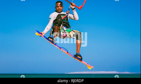 Egitto, Hurghada - 30 Novembre, 2017: Close-up kitesurfer sulla tavola da surf tenendo il kite strisce. Il vertiginoso aumento del volo nel cielo blu sopra il mare rosso superficie. Sport estremo attività. Foto Stock