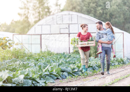 Famiglia sorridente con verdure in cassa a piedi dai cavoli cappucci a livello di azienda Foto Stock