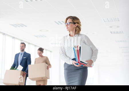Imprenditrice che trasportano i file mentre si colleghi a parlare con scatole di cartone al nuovo ufficio Foto Stock