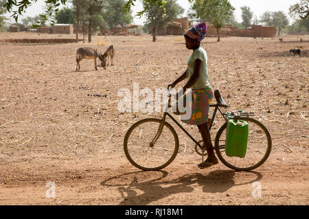 Il villaggio di Samba, Provincia Yako, Burkina Faso: una ragazza adolescente trasporta due taniche di acqua dal bene alla sua casa il suo moto. Foto Stock
