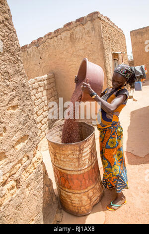 Villaggio Kourono,Yako provincia, Burkina Faso. Mariam Tougma, 23, versando il sorgo ha appena si sono dissolte in un vecchio tamburo di petrolio per memorizzare per conservarli nella sua famiglia composto. Foto Stock