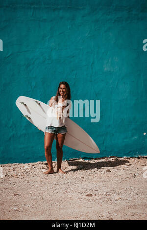 Felice surfer girl con tavola da surf nella parte anteriore della parete di blu Foto Stock