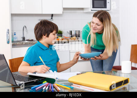 Donna sorridente dando il pranzo a suo figlio di fare i compiti kitche Foto Stock