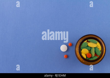 Pillole colorate su sfondo azzurro accanto ad una bottiglia di vetro contenente farmaci. Farmaci per uso nell'uomo. Foto Stock