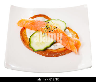 Deliziosi toast con salmone affumicato, cetriolo e salsa cremosa con verdi servita su piastra bianca. Isolato su sfondo bianco Foto Stock