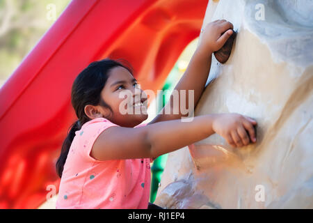 Ragazza indiana con un sorriso sul suo viso è tenuta su di un muro di roccia da scalare e guardare avanti alla sfida fisica. Foto Stock