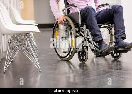 Sezione bassa di uomo seduto su una sedia a rotelle all'ospedale corridoio Foto Stock