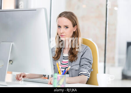 Ritratto di creative imprenditrice utilizzando computer desktop in ufficio Foto Stock