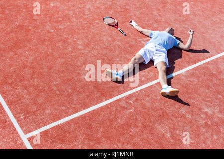 Lunghezza completa di deluso uomo maturo giacenti da racchetta da tennis su corte durante la stagione estiva Foto Stock